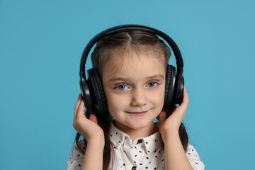 Portrait of cute little girl in headphones listening music on light blue background