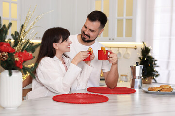 Happy couple in pajamas with hot drink and pastries together in kitchen decorated for Christmas