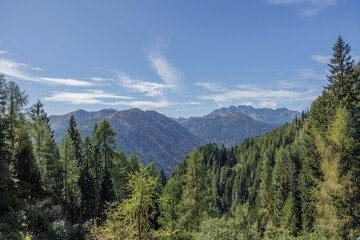 Obraz premium vista panoramica in alta quota su di un ambiente naturale tra le verdi foreste e le montagne Italiane della Val Pesarina, in Friuli Venezia Giulia, di giorno, con meteo sereno, in autunnno