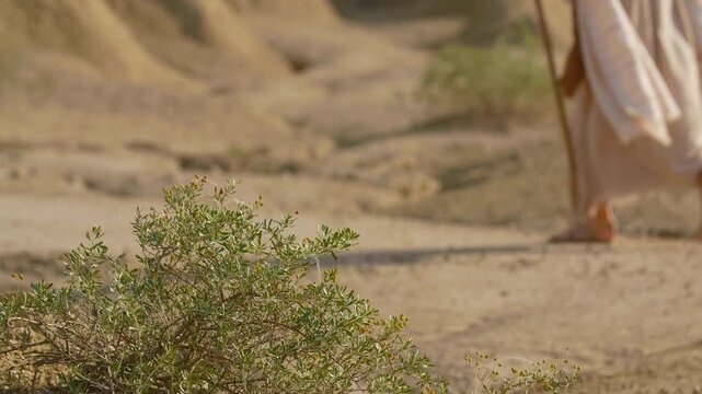 Man in biblical-inspired attire traveling through a barren, textured desert landscape under a clear sky. An inspiring scene of quiet resilience and determination in an isolated natural setting.