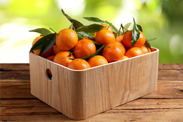 Fresh juicy tangerines in crate on wooden table against blurred green background