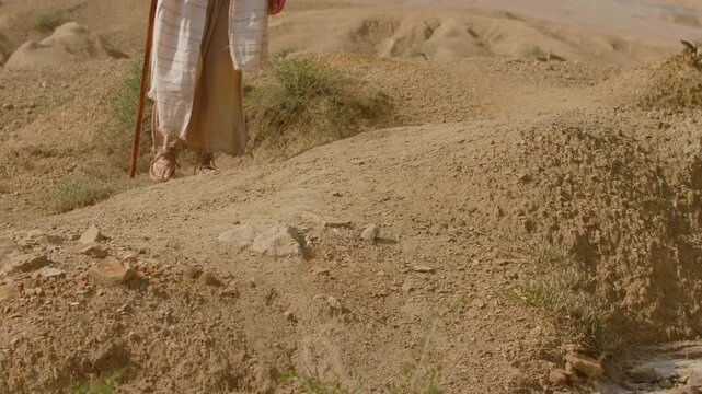 Sandaled feet move slowly across the arid terrain. Christian and spiritual concept. Slow motion shot