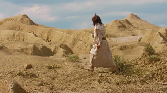 Representation of Christ in ancient-style clothing walks through a barren desert landscape, surrounded by sculpted sand formations and warm golden light. Cinematic scene evoking spirituality