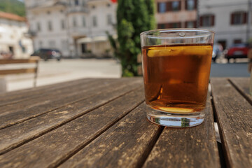 bicchiere riempito con del té alla pesca fresco, sopra un tavolo di legno, di giorno, in estate, in un ambiente urbano 