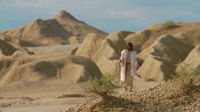 Depiction of Messiah, dressed in traditional white robes, explores an austere and sculptural desert environment. The earthy tones of the natural formations evoke a sense of temptation.