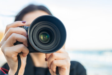 Low-angle view of a female photographer holding a professional camera against the blue sky, capturing outdoor moments and focusing on creative photography.