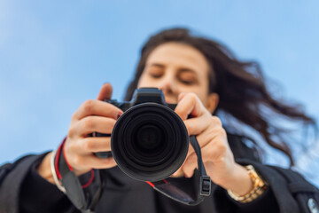 Low-angle view of a female photographer holding a professional camera against the blue sky, capturing outdoor moments and focusing on creative photography.