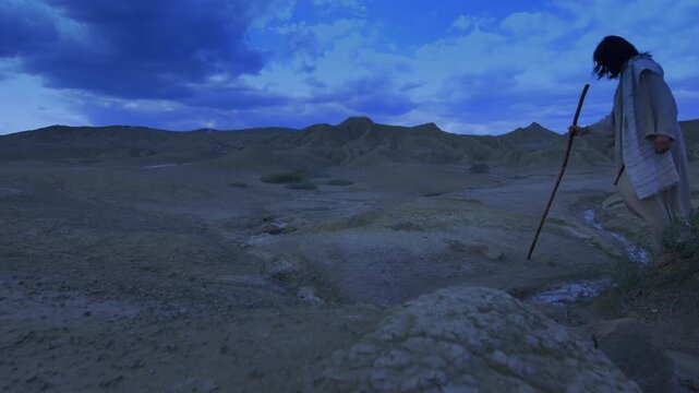 Christ alone wearing ancient robe crossing a barren and rugged landscape at night. Dramatic blue sky, emphasizing the isolation of the spiritual journey.
