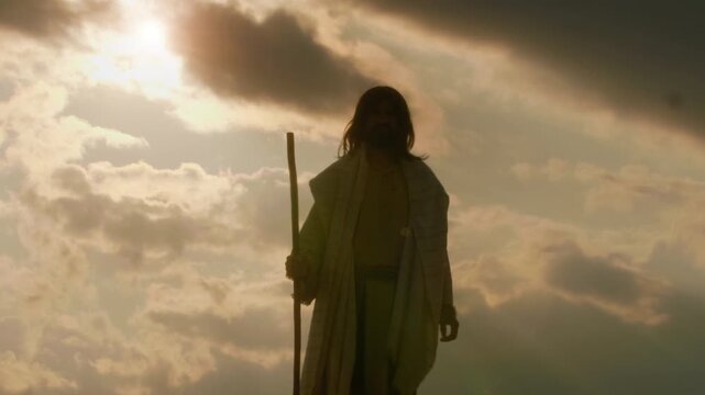 The solitary figure of the Christ in ancient robes standing atop a barren hill, arms raised wide in a gesture of deep prayer, adoration and spiritual triumph over the surrounding wilderness.