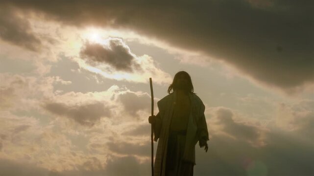 The solitary depiction of the Messiah in ancient robes standing atop a barren hill, arms raised wide in a gesture of deep prayer, adoration and spiritual triumph over the surrounding wilderness.