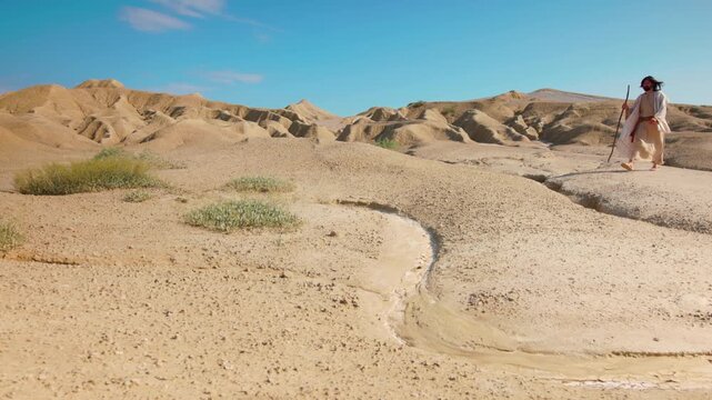 A robed Traveler takes steady steps across the rugged Desert of Judea. Christian and spiritual concept