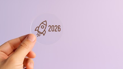 Hand holding transparent circle with rocket icon and 2026 year text on purple background, business startup and new year concept, Business Launch, Future Vision, Strategic Planning, Timeline Milestone