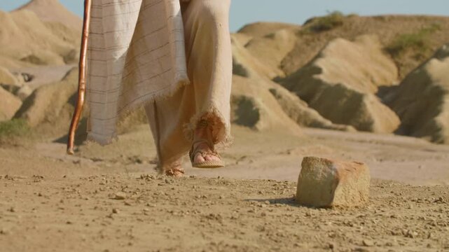 A wanderer in ancient-style clothing stepping across a dusty desert path. Christian and spiritual concept. Slow motion Shot
