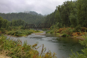 photo of railroad bridge crossing a river in the forest during a rainstorm with rain drops falling on the stream