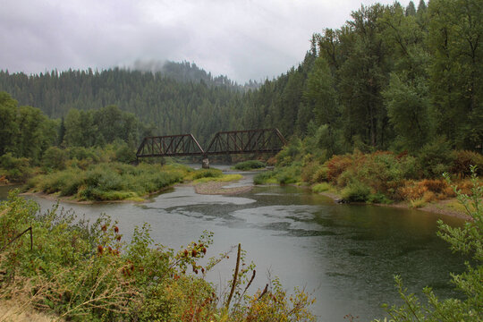 photo of railroad bridge crossing a river in the forest during a rainstorm with rain drops falling on the stream