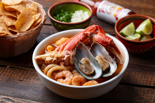 Mexican seafood soup with shrimp, mussels and crab served with tortilla chips and lime, rustic seafood stew on wooden table