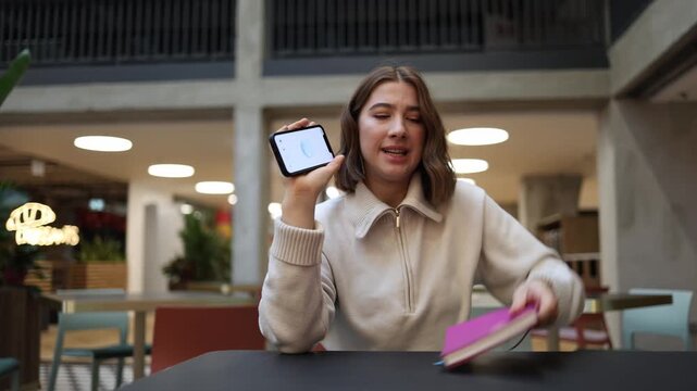 Angry woman slams her notebook on the table after receiving yet another wrong answer from artificial intelligence gripping her phone with frustration in a bright modern cafe