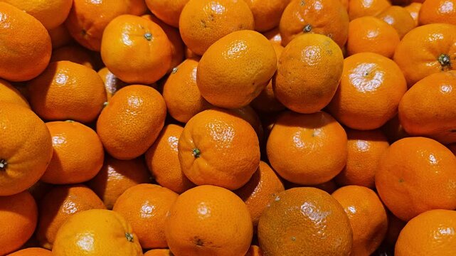 A close-up view of a large pile of bright, ripe, and vibrant orange Clementine or mandarin fruits, showing the rich color and textured skins in bulk.