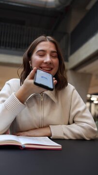 Vertical screen a young screenwriter consults artificial intelligence while drafting her film script smiling at her phone as she refines dialogue ideas during a creative break with her open notebook 