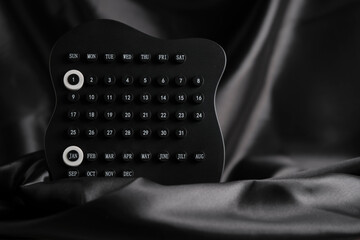 Sleek black desk calendar with January and 1st highlighted rests on smooth black fabric, creating an elegant minimal scene.