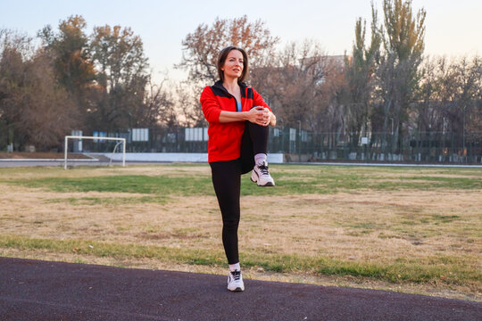 Fit Middle-Aged Woman Doing Standing Knee Hug Exercise Outdoors