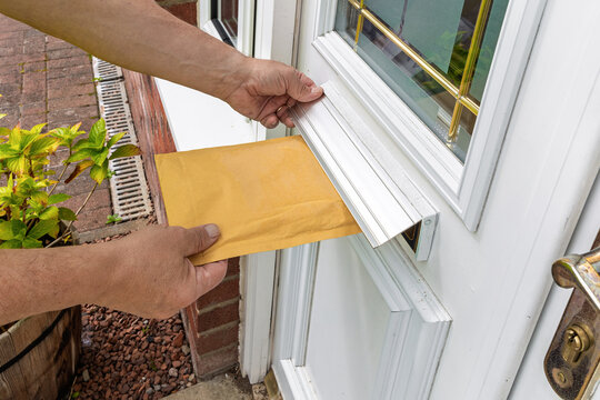 Postal Worker in High-Visibility Vest Delivering Bubble Mailer Through Door Slot