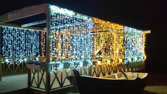 On the Şark&ouml;y coast, a wooden gazebo decorated with two-colored string lights, and next to it a small fishing boat.