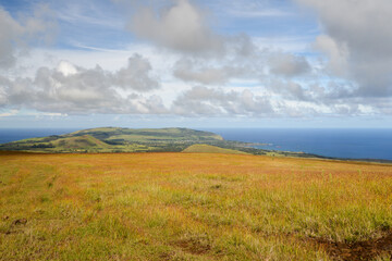Grassy plains leading to hills and ocean under a cloudy sky