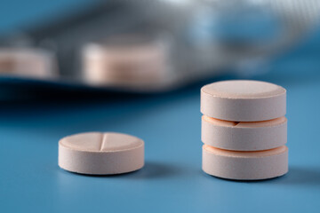 A stack of pills on a blue surface. One pill on the side. The pills are pink and there is a blister...