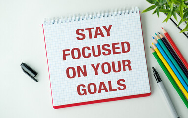 A red spiral bound notebook with the words Stay Focused on Your Goals written on it.
