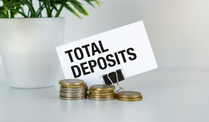 A white card with the words Total Deposits written on it. The card is attached to a stack of coins