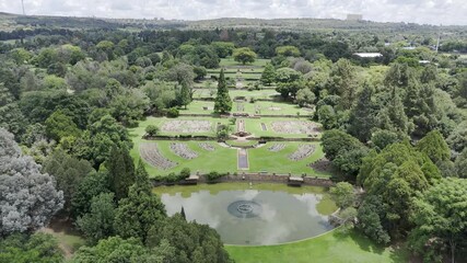 Drone flies backwards and to the left at edge of botanical gardens on partially cloudy day in Randburg, Johannesburg, South Africa