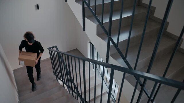 High angle view of a courier walking up the stairs in an apartment building with a package