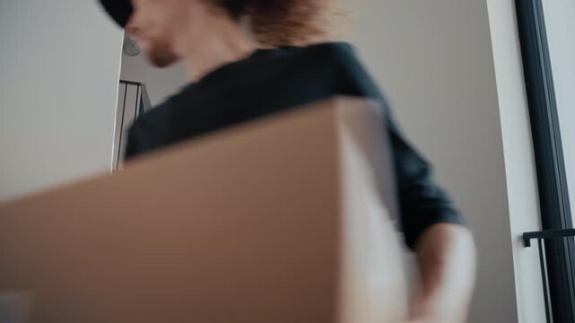 Young courier delivering a cardboard box walking down the stairs of an apartment building