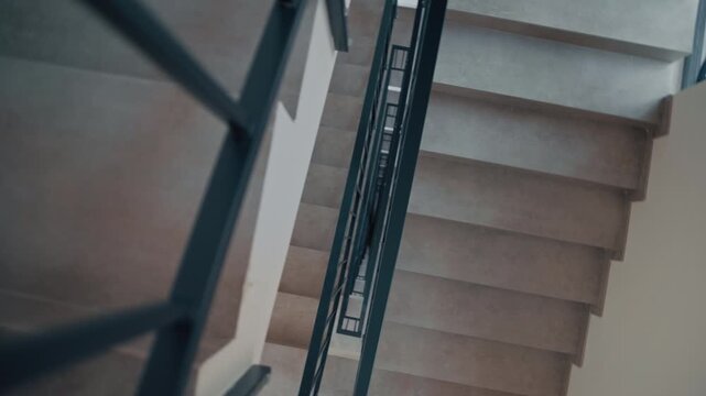 Dynamic composition where a delivery man in black uniform moves through the geometric structure of a concrete stairwell, package in hand.