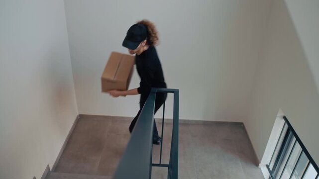 Courier wearing a black uniform and a cap delivering a package walking up a concrete staircase