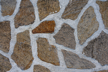 Textured background of a stone wall made from uneven, natural rocks embedded in light cement mortar. 