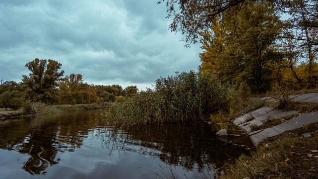 Autumn riverbank under heavy clouds and silent trees  - Powered by Adobe
