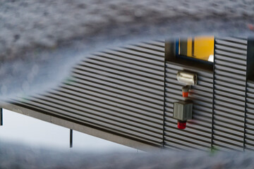 Security alarm reflected in a puddle with industrial metal facade