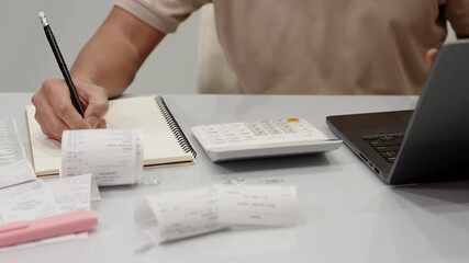 Close-up of man calculating monthly expenses at home desk with receipts, notebook, calculator and laptop. Personal finance planning in clean modern workspace. Effort to keep track of expenses at home.