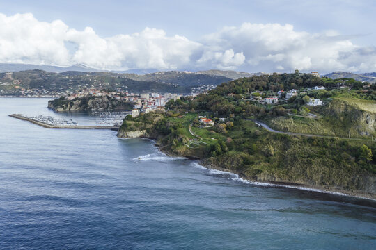 Aerial view of the craggy coastline where the sapphire sea meets the green bluffs, and Agropoli's buildings nestle against distant hills, Agropoli, Campania, Italy.