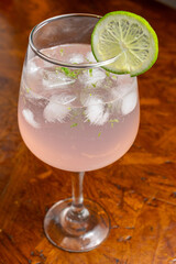 Pink Gin Tonic Spritz cocktail with a slice of lime and ice in a balloon glass on a rustic wooden table
