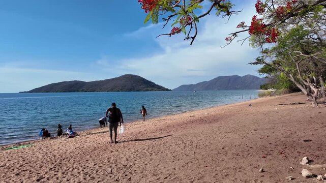 Cape Maclear  Lake Malawi Africa. 01, 12.2025. Video.  Holidaymakers on the sandy beach at Cape Maclear within the Malawi National Park ssouthern Malawi Africa.