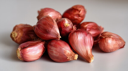 Pile of fresh red shallots on a light grey background, showcasing their vibrant color and texture, ready for culinary use.