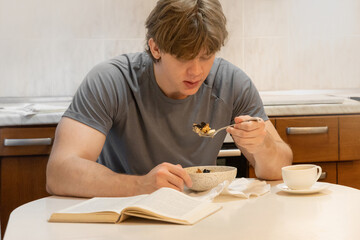 Young caucasian man eating breakfast while reading book in home kitchen interior, indoor calm morning routine, lifestyle and relaxation concept. Morning Kitchen Routine: Cooking Oatmeal and Coffee