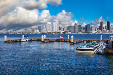 2025-11-28 DOWNTOWN SAN DIEGO SKYLINE WITH SEAPORT VILLAGE THE CONVENTION CENTER AND THE RANY SHELL FROM CORANADO ISLAND WITH A SMALL DOCK AND A NICE SKY WITH PUFFY CLOUDS