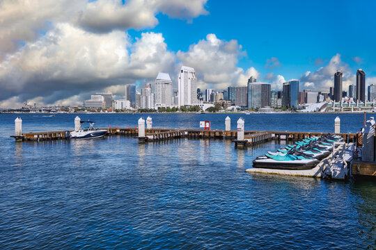 2025-11-28 DOWNTOWN SAN DIEGO SKYLINE WITH SEAPORT VILLAGE THE CONVENTION CENTER AND THE RANY SHELL FROM CORANADO ISLAND WITH A SMALL DOCK AND A NICE SKY WITH PUFFY CLOUDS