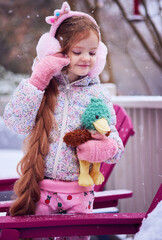 Winter Portrait of Smiling Little Girl in Fluffy Earmuffs Holding Plush Duck Toy During Gentle Snowfall &ndash; Cozy Pastel Childhood Moment While Playing Outdoor