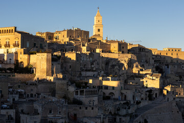 Obraz premium the iconic matera cathedral bell tower and historic sassi buildings perched on the hillside, illuminated by the warm, directional light of a clear sunset or sunrise