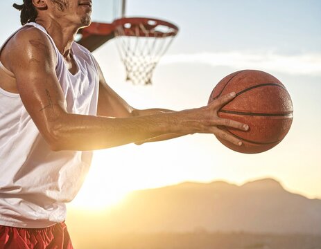 A focused male basketball player holding the ball with both hands on an outdoor court at sunset. - Powered by Adobe